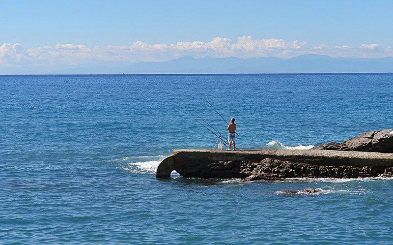 A man is fishing from stones next to the sea in Recco